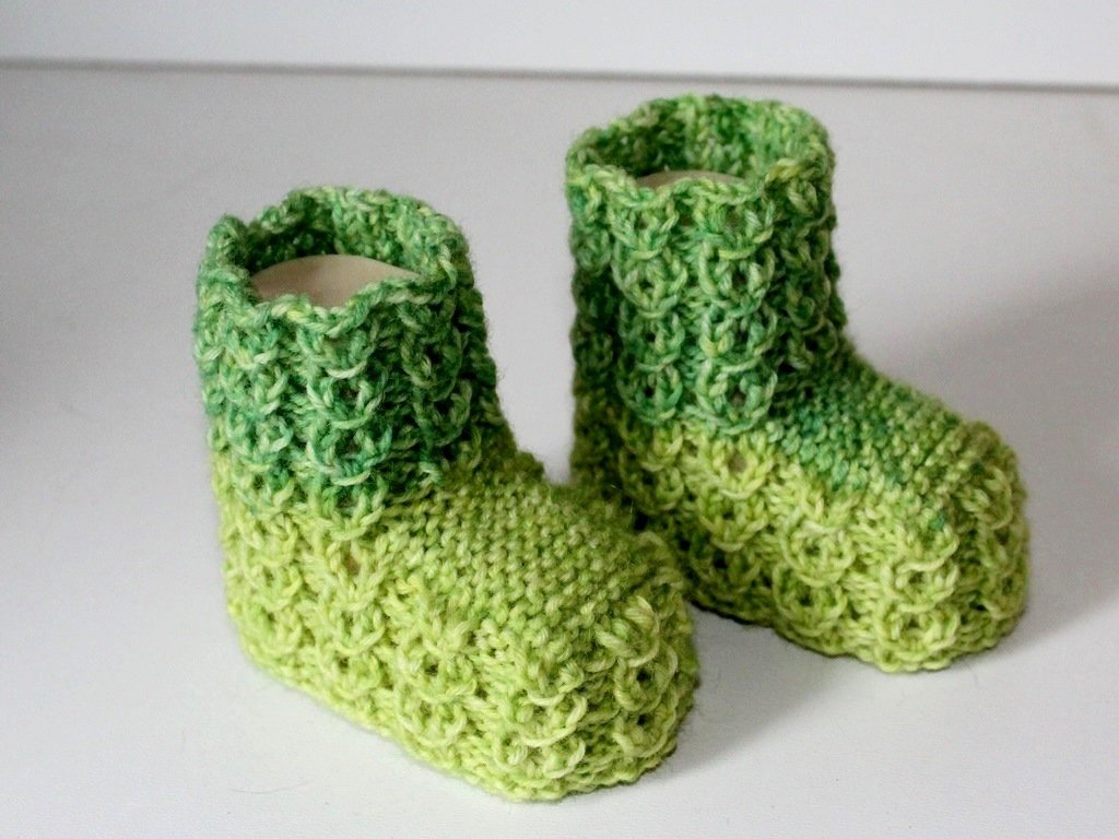 Gestrickte grüne Babyschuhe mit Farbverlauf und Strukturmuster auf hellem Untergrund