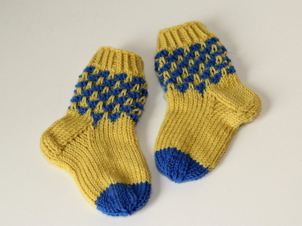 Handgestrickte gelb-blaue Babysocken auf hellem Hintergrund.