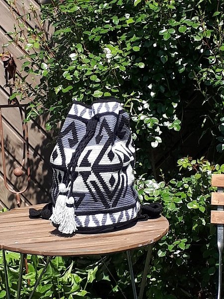 Gehäkelter Rucksack mit schwarz-weiß-grauem geometrischem Muster und weißen Quasten auf Holztisch