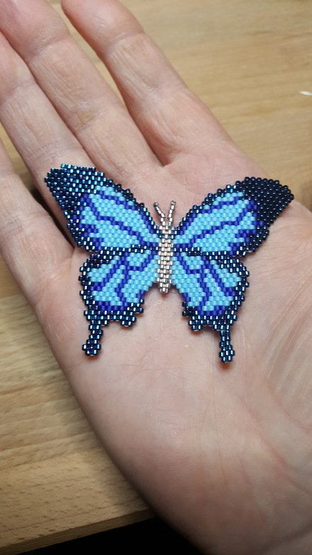 Blauer Perlen-Schmetterling als Anhänger liegt auf einer Hand