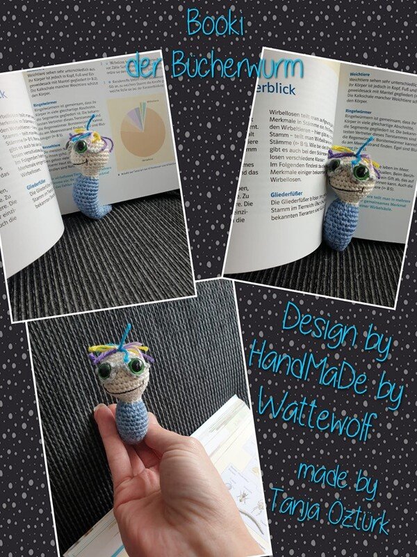 Gehäkeltes Amigurumi-Lesezeichen in Bücherwurm-Form mit blauem Körper, großen grünen Augen und bunten Fäden, zwischen Buchseiten gesteckt.