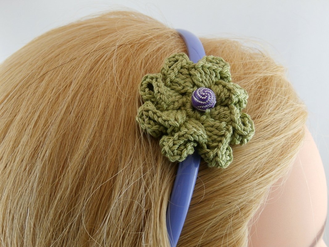 Gehäkelte olivgrüne Blume mit lila Knopf auf lila Haarreif im blonden Haar