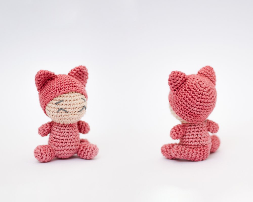 Zwei rosa gehäkelte Amigurumi-Katzen, eine von vorne mit lächelnder Miene, die andere von hinten.