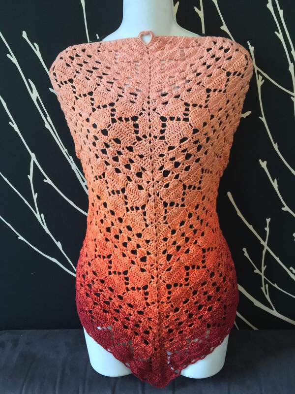 Gehäkeltes Dreieckstuch in Ombre-Farben von Lachsrosa zu Weinrot mit Lochmuster und Herzdetail auf einer Schneiderpuppe.