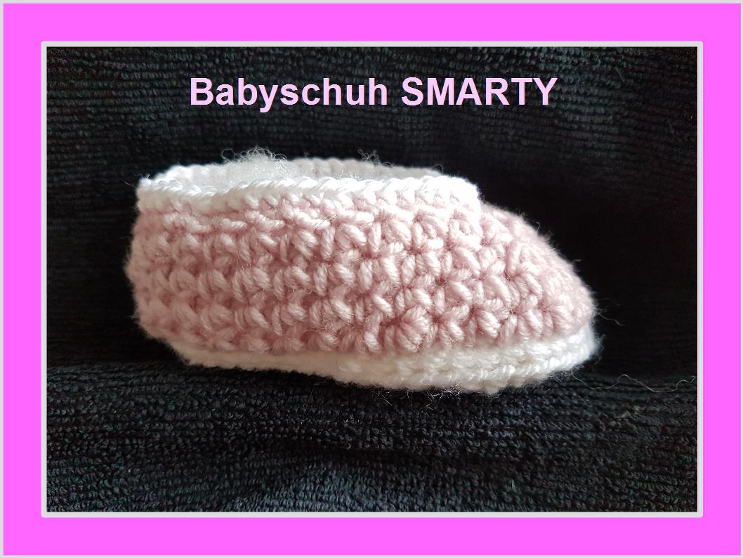 Gehäkelter Babyschuh in Rosa und Weiß auf dunklem Hintergrund
