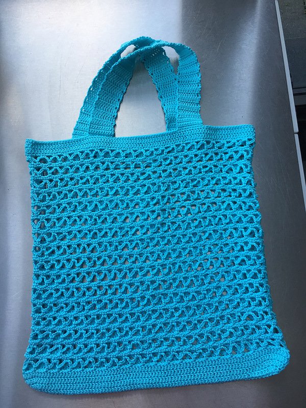 Türkise gehäkelte Netztasche mit breiten Henkeln auf metallischer Fläche