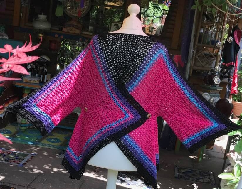 Gehäkelte Damenjacke auf einer Schaufensterpuppe in Pink, Schwarz und Blau mit weiten Ärmeln.