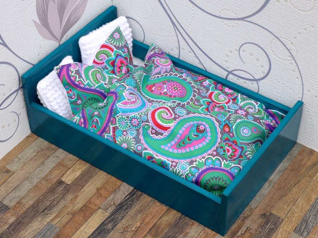 Miniatur-Puppenbett mit türkisfarbenem Rahmen, Paisley-Bettwäsche und weißen Kissen.