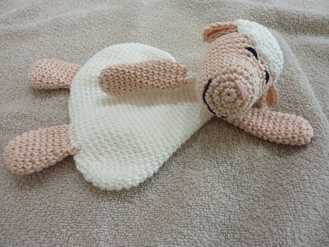 Gehäkeltes Schmusetuch in Schaf‑Form liegend mit cremeweißem Körper und roséfarbenem Kopf und Pfoten