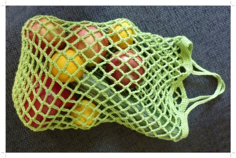 Hellgrünes gehäkeltes Einkaufsnetz mit Äpfeln, Zitronen und Gurke