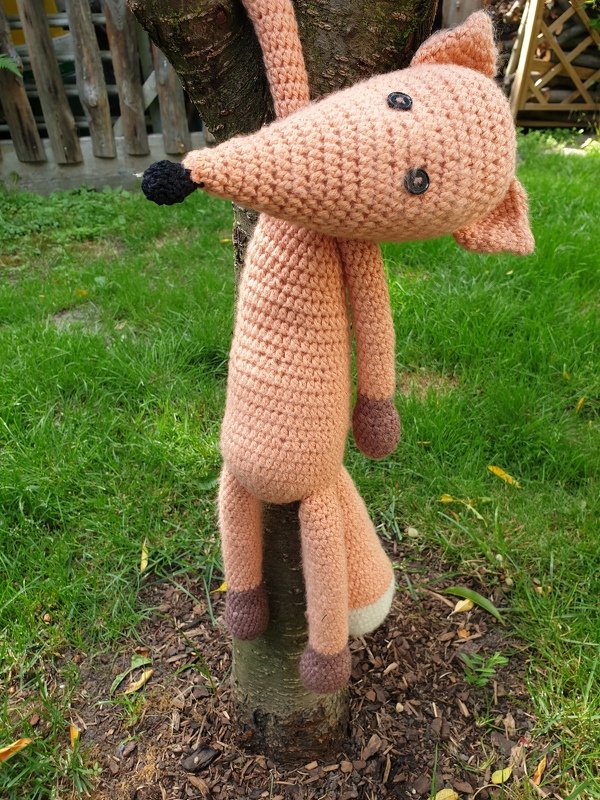 Gehäkelter Amigurumi-Fuchs in Pfirsich hängt an einem Baumstamm