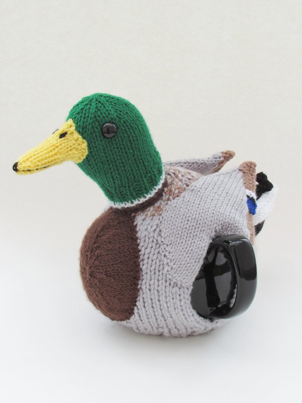 Knitted duck-shaped mug cozy with green head and yellow beak on a handled mug