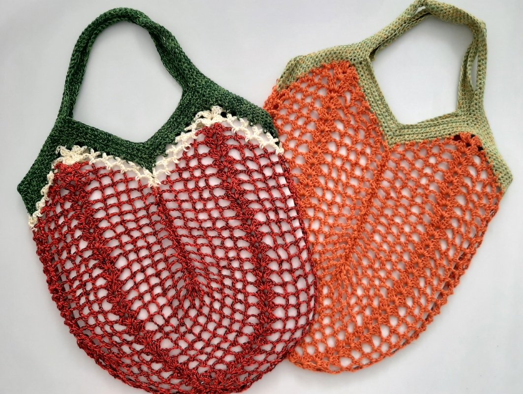 Zwei gehäkelte Netztaschen in Rot und Orange mit grünen Henkeln auf hellem Hintergrund