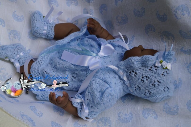 Baby in hellblauem gestricktem Set mit Mütze, Jäckchen und Schühchen, liegend