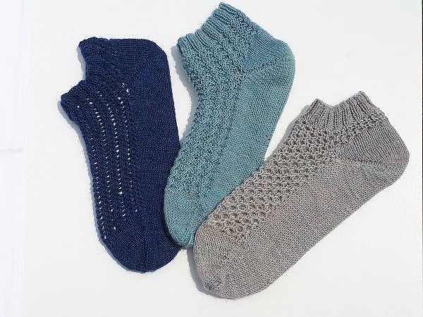 Drei kurze gestrickte Socken nebeneinander in Blau, Türkis und Grau