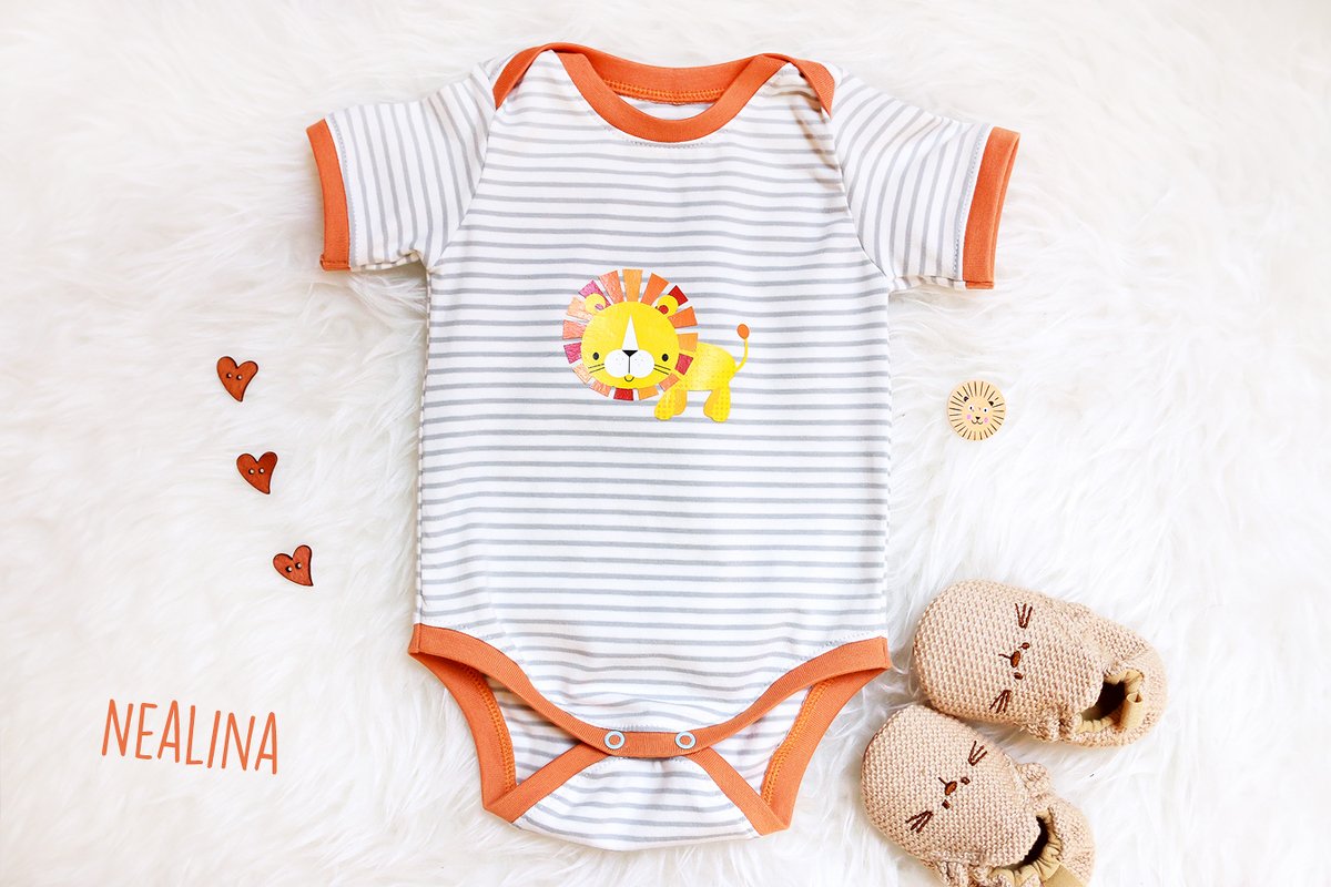 Gestreifter Kurzarm-Body mit orangefarbenen Bündchen und Löwen-Applikation auf hellem Fell, neben gestrickten Babyschuhen und Herzknöpfen