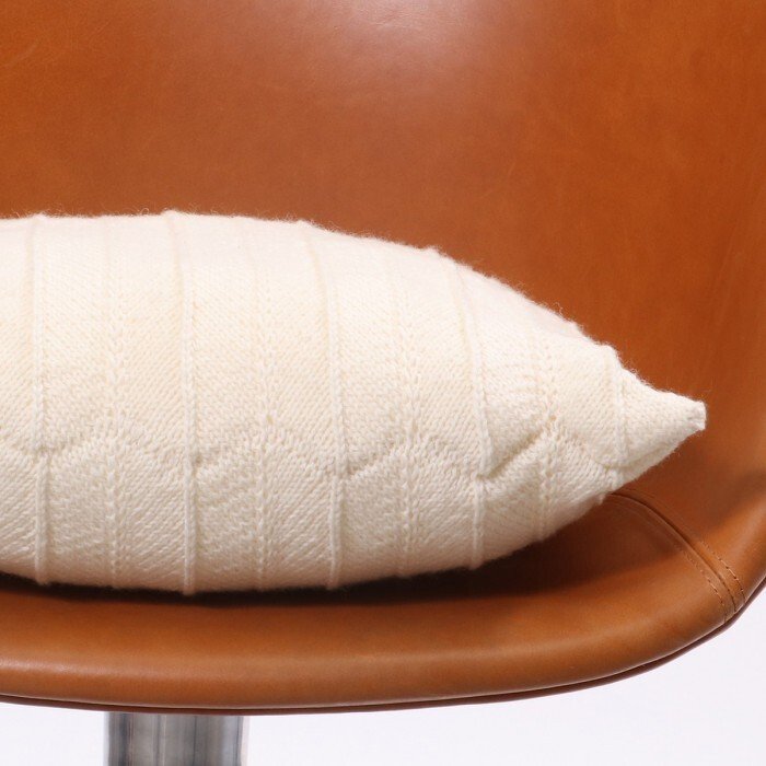 White rectangular knitted lumbar pillow with chevron texture on brown leather chair