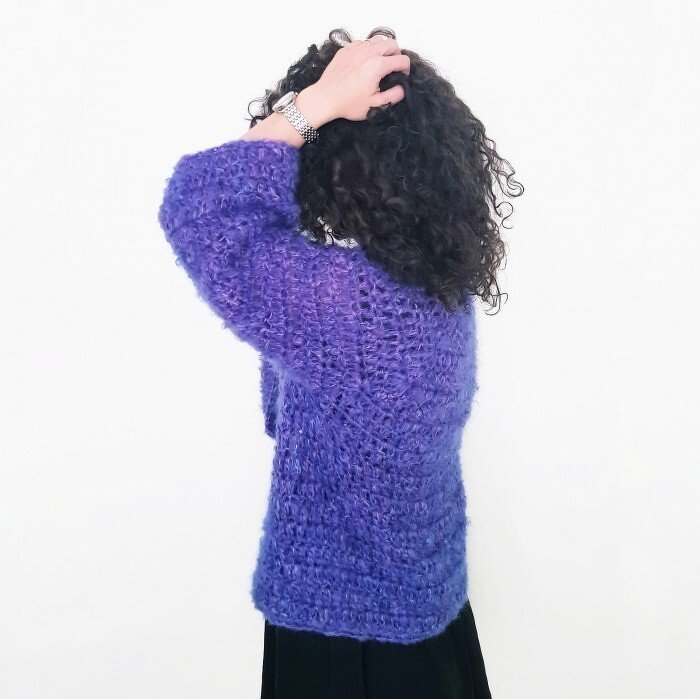 Back view of a woman wearing a purple fuzzy open-stitch crochet cardigan