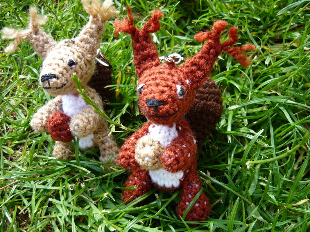 Zwei gehäkelte Amigurumi-Eichhörnchen mit Eicheln und Schlüsselringen auf Gras