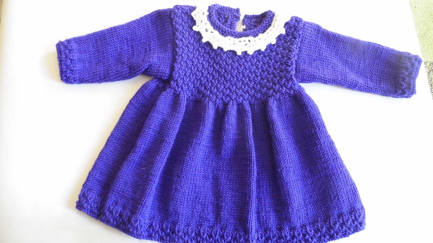 Gestricktes violettes Babykleid mit langen Ärmeln und weißem gehäkeltem Kragen, flach ausgelegt