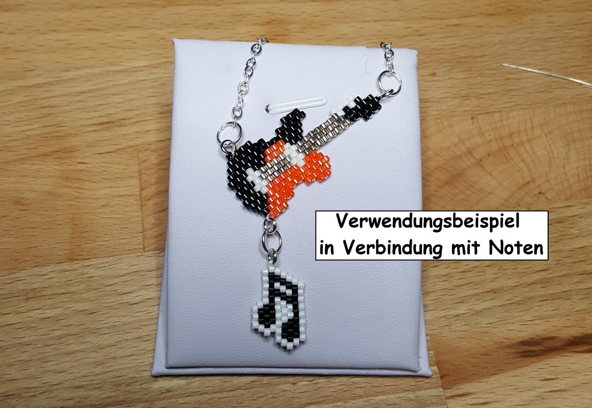 Perlenanhänger in Gitarrenform mit kleinem Notenanhänger auf weißem Display, silberfarbene Kette; Textoverlay 'Verwendungsbeispiel in Verbindung mit Noten'.