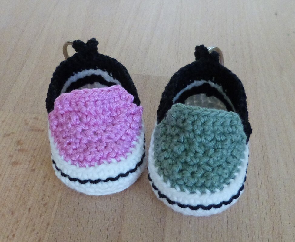 Zwei gehäkelte Mini-Sneaker-Schlüsselanhänger in Rosa und Grün auf Holzuntergrund