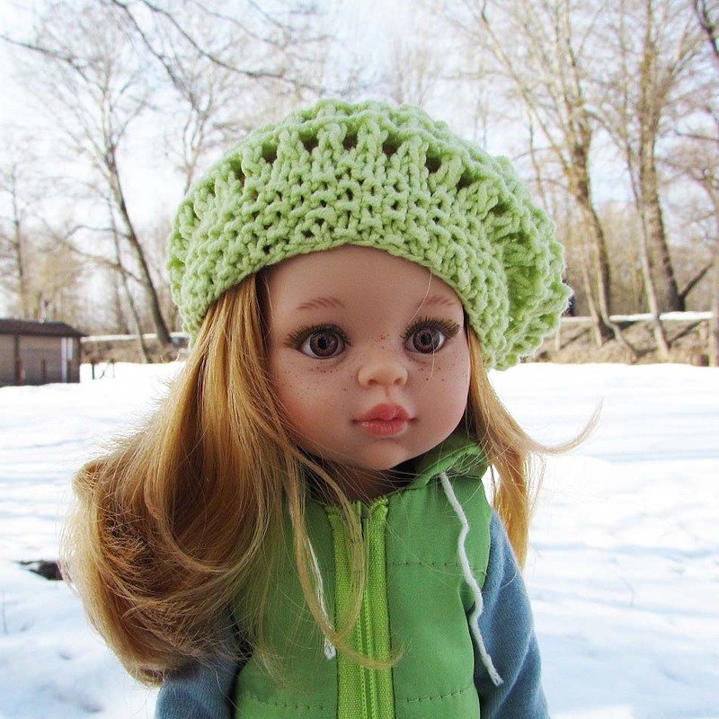 Close-up of a doll wearing a textured light green knit-look hat outdoors in winter.