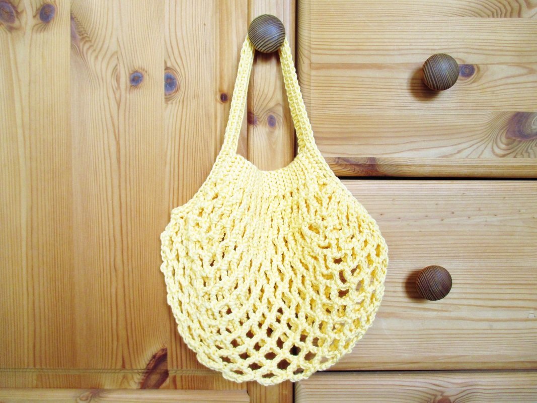 Gelbe gehäkelte Netztasche mit kurzem Henkel, an Holzknauf hängend