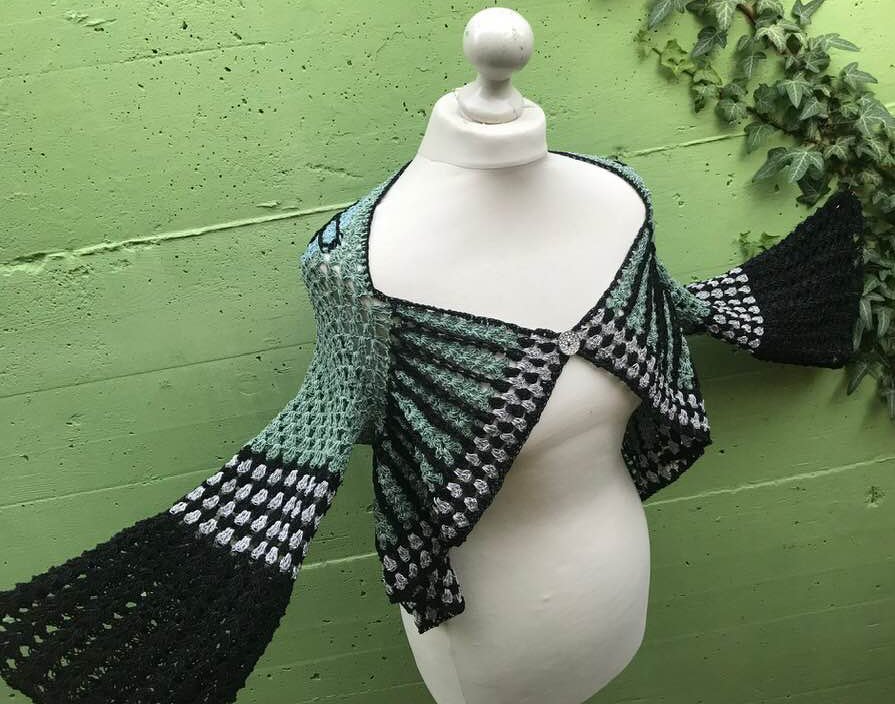 Kurze gehäkelte Damenjacke in Mint, Schwarz und Grau auf Schaufensterpuppe mit weitem Ärmelschnitt