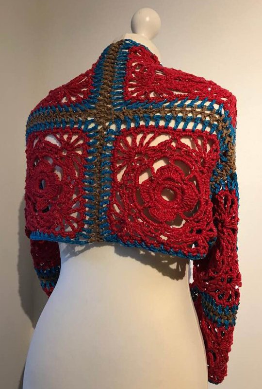 Rückansicht eines gehäkelten Boleros aus Granny‑Squares in Rot, Türkis und Braun auf einer Schaufensterpuppe.