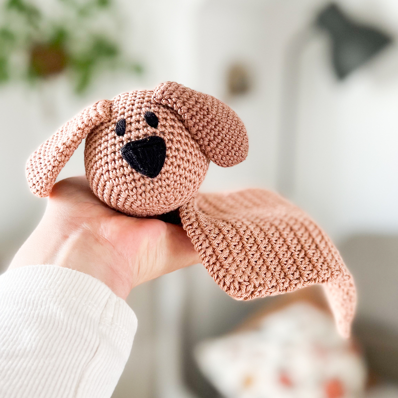 Close-up of a small crochet dog snuggle blanket held in a hand to show size and stitch texture