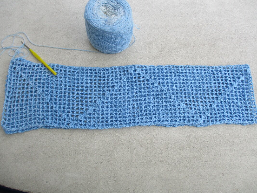 Hellblauer gehäkelter Loop im offenen Netzmuster mit Garnknäuel und gelber Häkelnadel