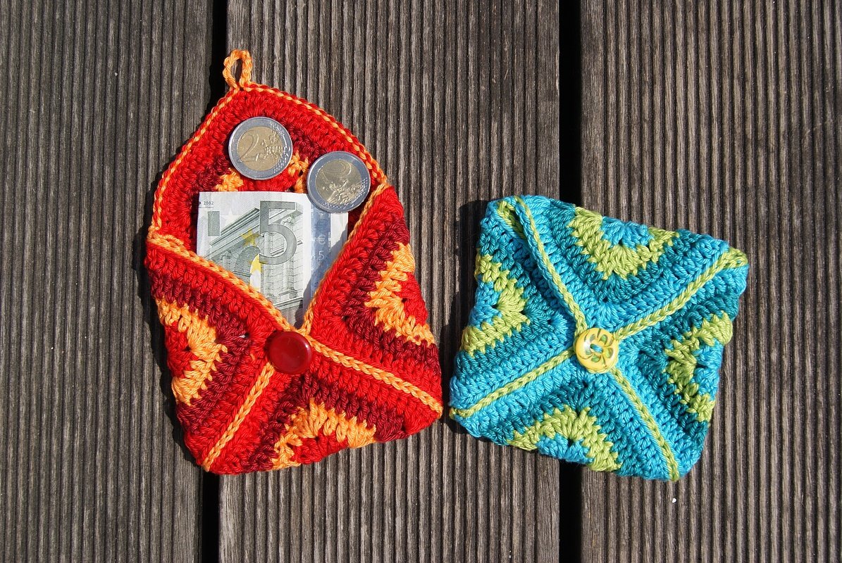 Gehäkelte Täschchen rot und blau-grün mit Münzen und Schein auf Holzdielen
