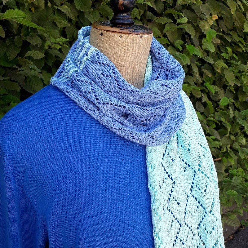 Gestrickter Schal in Blau- und Minttönen mit Rauten-Lochmuster, drapiert auf einer Schaufensterpuppe.
