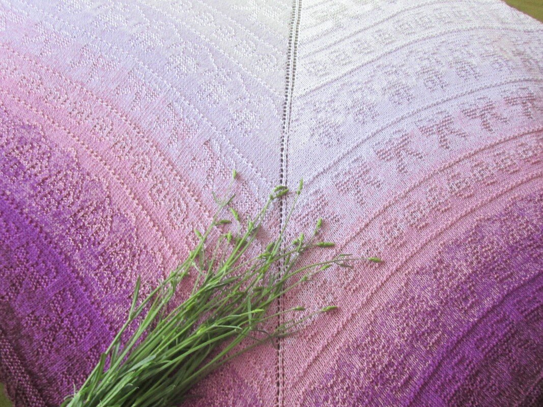 Gestricktes Dreieckstuch in Rosa- und Lilatönen mit texturierten Mustern und grünen Grashalmen