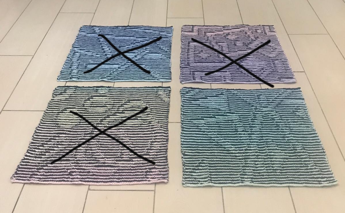 Vier gestrickte Musterproben mit Farbverläufen und Streifen auf hellem Fliesenboden, drei mit schwarzem X markiert
