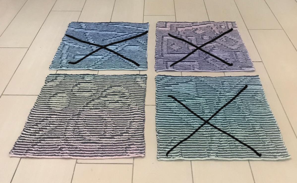 Vier quadratische Strickproben auf hellem Boden, drei mit schwarzem X, eine ohne Markierung