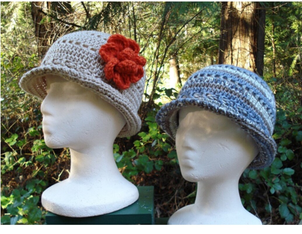 Two crocheted cloche hats on mannequin heads: beige with an orange flower, and blue-brown striped.