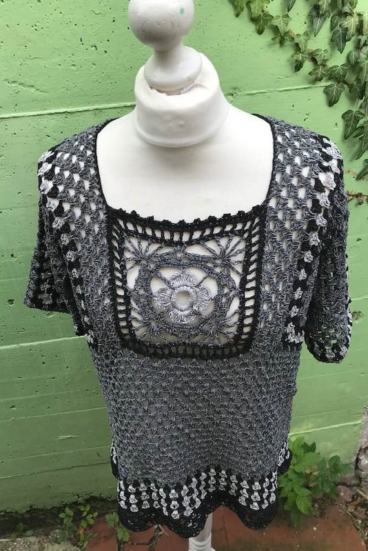Gehäkeltes grauschwarz-weißes Damen‑Shirt mit quadratischem Spitzen‑Motiv am Ausschnitt auf Schaufensterpuppe