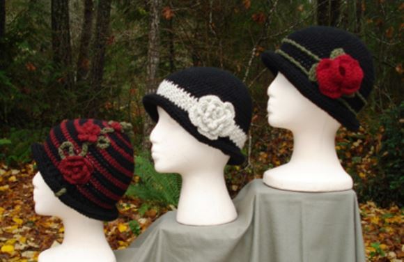 Three black crocheted cloche hats on mannequin heads with red, cream, and olive floral accents outdoors