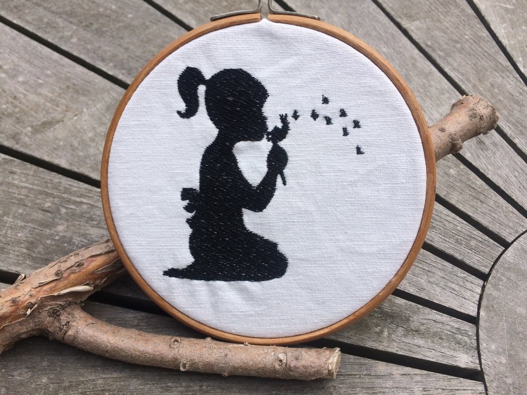 Gestickte schwarze Silhouette eines knienden Mädchens mit Pusteblume im Holz-Stickrahmen