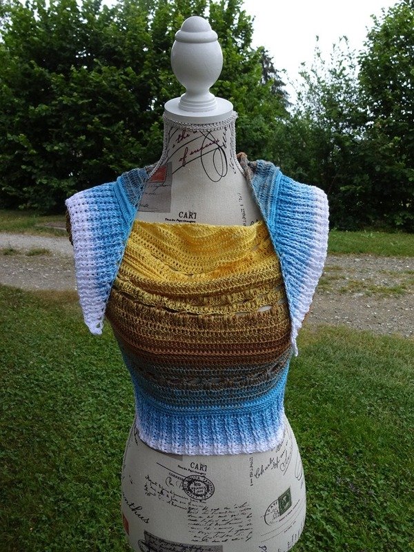 Gehäkeltes Halbrundtuch in Gelb, Braun, Blau und Weiß auf einer Schneiderpuppe im Garten