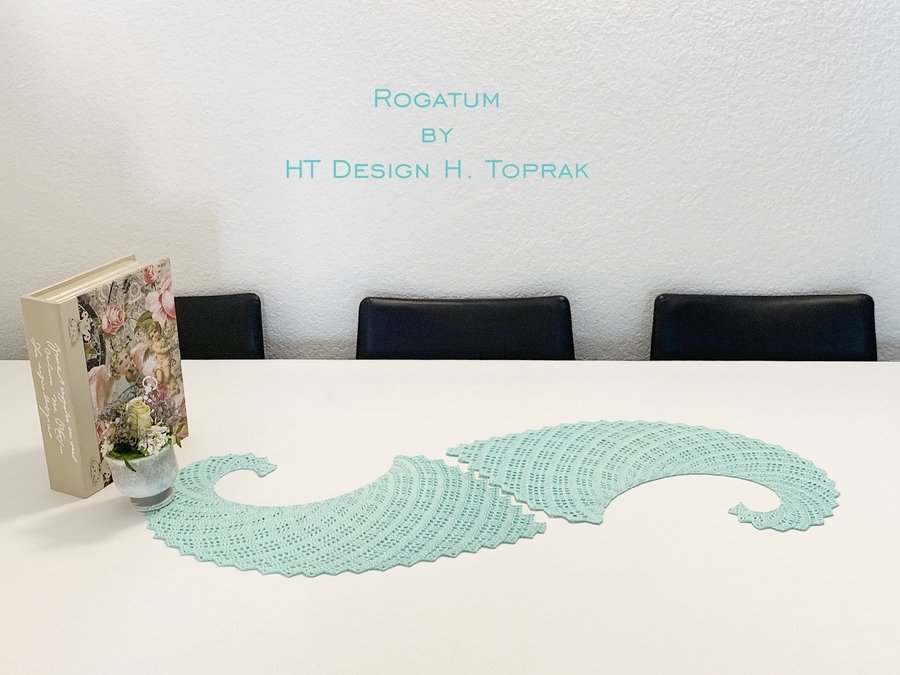 Two mint-green crocheted doilies with wavy openwork on a white table beside a book and a small potted plant.