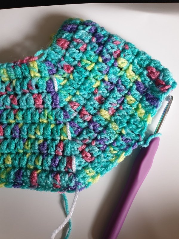 Gehäkelter Baby-Pullover in Türkis mit bunten Farbverläufen und lila Häkelnadel
