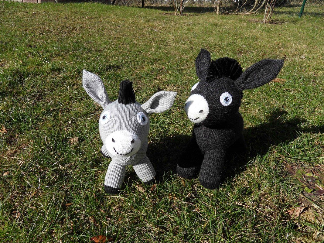 Zwei gestrickte Amigurumi-Esel, ein grauer und ein schwarzer, auf Gras