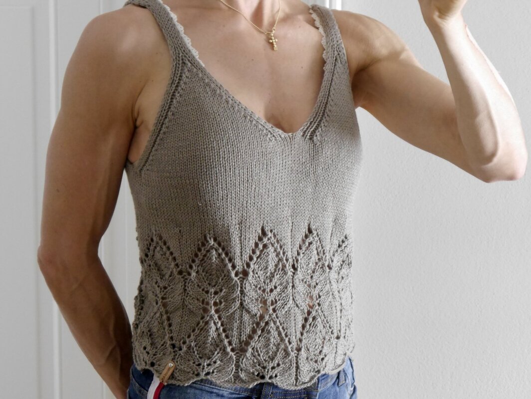 Woman wearing a beige knitted V-neck tank top with a lace lower panel and scalloped hem