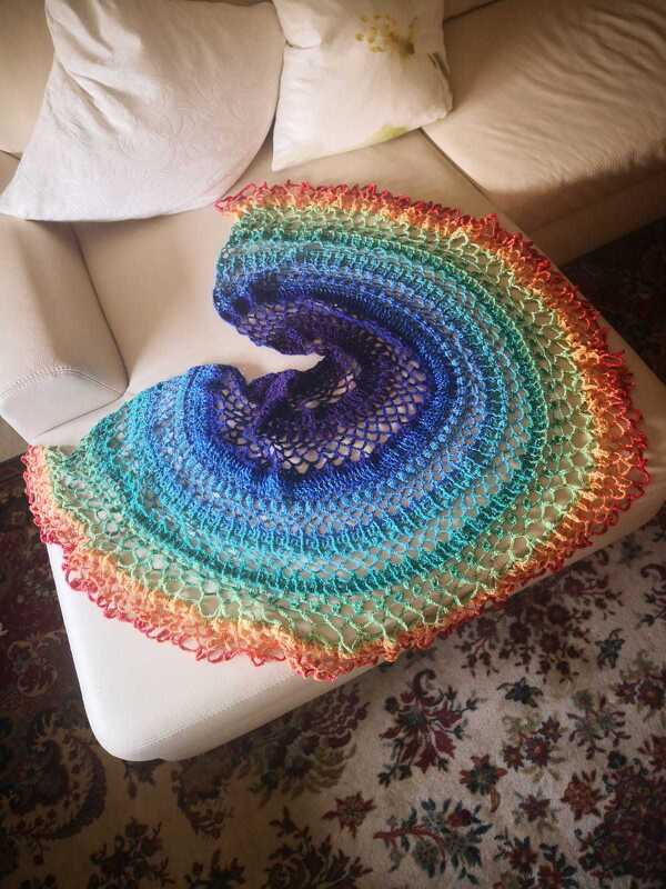 Gehäkeltes halbrundes Tuch mit Regenbogenverlauf auf cremefarbener Couch