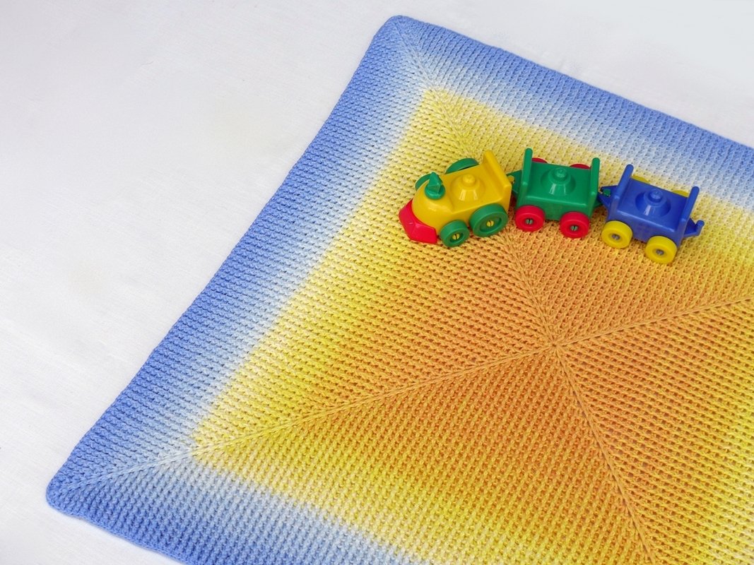 Quadratische gehäkelte Decke mit Farbverlauf und kleinem Kunststoff-Spielzug