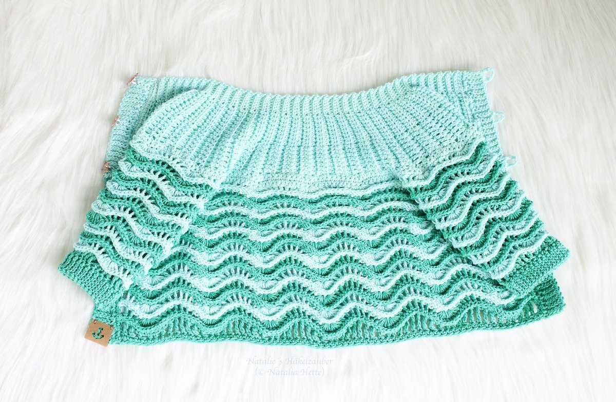 Folded mint-green crochet baby jacket with ribbed yoke and wavy ruffled body on white faux fur