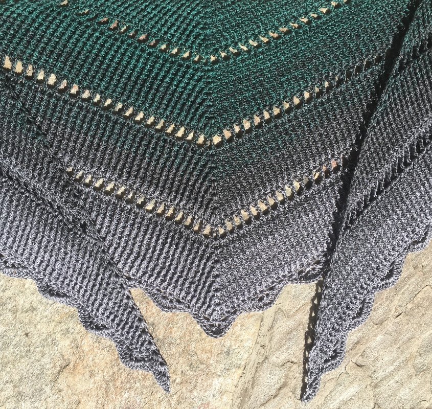 Close-up of textured crochet triangle shawl showing eyelet rows and scalloped hem in green and gray